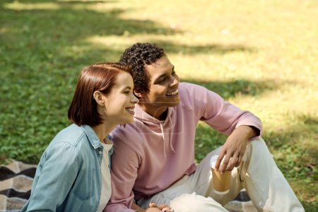 Ein stilvoller verliebter Mann und eine verliebte Frau sitzen auf einer bunten Decke und genießen einen friedlichen Moment in einem Rasenpark.