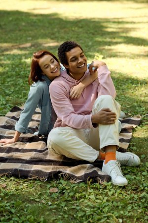 Ein Mann und eine Frau in lebendiger Kleidung sitzen auf einer Decke im Gras und genießen einen friedlichen Moment zusammen im Freien.