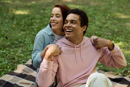 Un hombre y una mujer en traje vibrante sentados en una manta juntos en un parque, disfrutando de un momento de paz juntos.