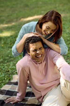 Téléchargez les photos : Un couple aimant, vêtu d'une tenue vibrante, se détendre dans un parc pendant que l'homme est assis sur le dessus de la femme sur une couverture colorée. - en image libre de droit