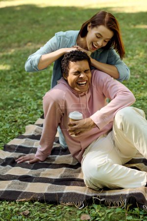 Un couple aimant et diversifié assis sur une couverture colorée dans un parc, partageant des moments intimes ensemble.