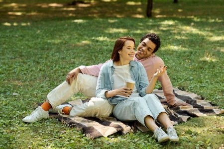 Téléchargez les photos : Un couple diversifié vêtu d'une tenue vibrante s'assoit sur une couverture dans l'herbe, profitant d'un moment paisible ensemble dans le parc. - en image libre de droit