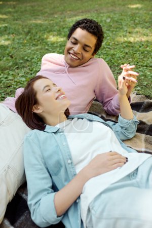 A man and a woman in vibrant attire lay together on a blanket in the grass, enjoying a relaxing moment in the park.
