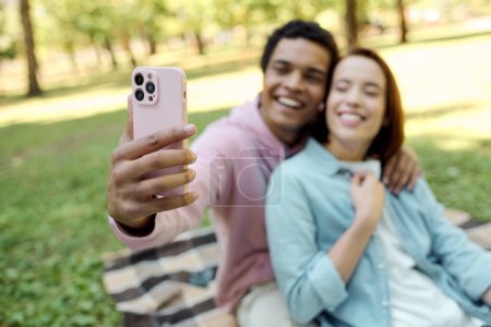 A diverse, loving couple in vibrant attire capture a moment of happiness together by taking a selfie in a beautiful park setting.