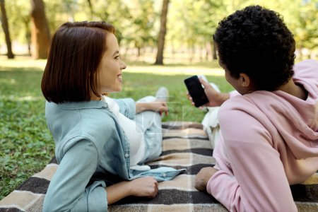 Téléchargez les photos : Couple aimant divers, vêtu de façon vibrante, assis joyeusement sur une couverture dans un cadre de parc. - en image libre de droit
