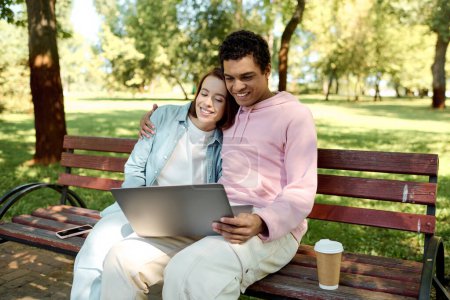 Téléchargez les photos : Un couple en tenue vibrante s'assoit ensemble sur un banc de parc, absorbé dans un écran d'ordinateur portable, profitant de l'autre compagnie. - en image libre de droit