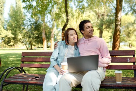 A man and woman, dressed in vibrant attire, sit on a park bench with a laptop, engrossed in online activities together.