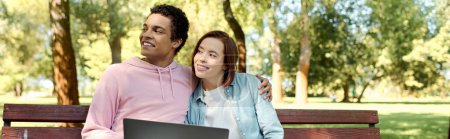 Téléchargez les photos : Un homme et une femme en tenue vibrante assis sur un banc de parc, absorbé dans un ordinateur portable, profiter d'un rendez-vous numérique. - en image libre de droit