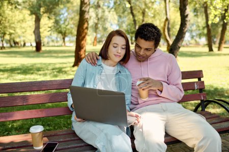 A man and woman in vibrant attire sit on a park bench, engrossed in a laptop screen, enjoying quality time together outdoors.