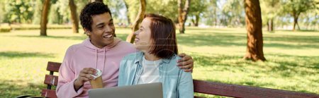 A diverse couple in vibrant attires sitting on a bench, working together on a laptop in a park setting.
