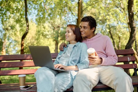 Photo for A stylish man and woman in colorful outfits sit on a bench, using a laptop outdoors in a park. - Royalty Free Image
