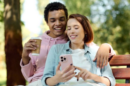 Foto de Una pareja diversa en traje vibrante se sienta en un banco, absorto en un teléfono celular juntos. - Imagen libre de derechos