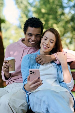 Diversa pareja en traje vibrante sentado en el banco del parque, absorto en la pantalla del teléfono celular.