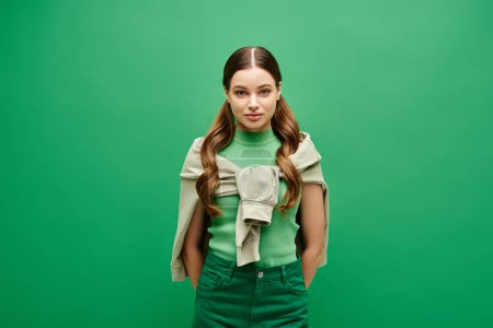 Téléchargez les photos : Une jeune femme aux cheveux longs se dresse sur un fond vert dans un décor de studio. - en image libre de droit