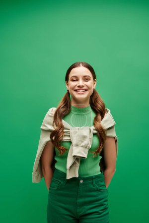 Téléchargez les photos : Une jeune femme dans la vingtaine se tient élégamment devant un fond vert vibrant dans un cadre de studio. - en image libre de droit