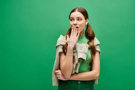 Photo for Shocked woman in her 20s poses confidently in front of a vibrant green background in a studio setting. - Royalty Free Image