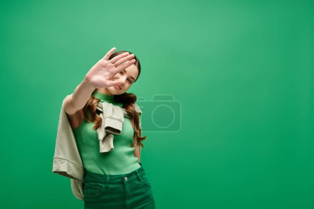 Foto de A woman in a green shirt hides her face in her hand, a gesture of vulnerability and introspection in a studio setting. - Imagen libre de derechos