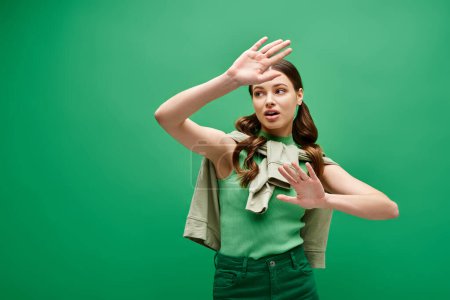 A young woman in her 20s, clad in a green shirt, gracefully makes a hand gesture in a studio setting.