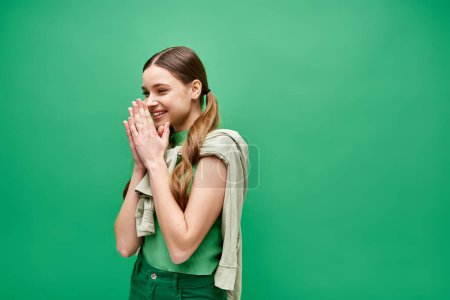 A happy young woman in her 20s stands confidently in front of a vivid green background in a studio setting.