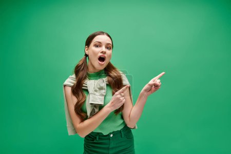 Eine junge Frau in ihren Zwanzigern, in einem grünen Hemd, zeigt mit neugieriger Miene auf etwas aus dem Off..