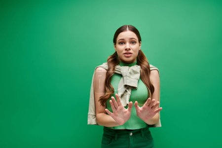 Photo for Scared young woman in her 20s stands in front of a vivid green background in a studio setting. - Royalty Free Image