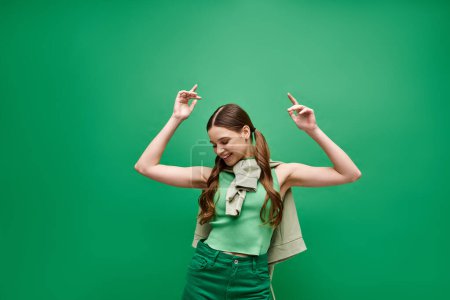 Téléchargez les photos : A stunning young woman in her 20s, wearing a matching green t-shirt and pants, poses in a studio setting, exuding grace and charm. - en image libre de droit