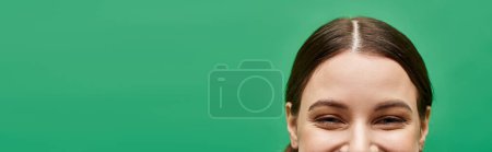 Photo for A young woman in her 20s smiles warmly against a vibrant green background in a studio setting. - Royalty Free Image