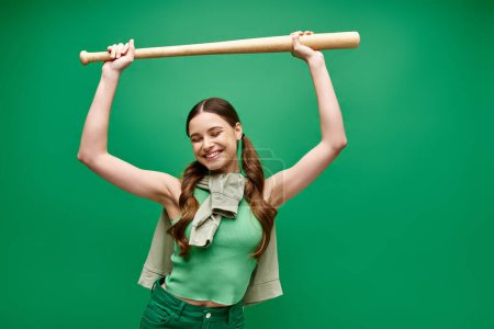 Téléchargez les photos : A young, beautiful woman in her 20s poses in a studio setting, defiantly holding a baseball bat over her head. - en image libre de droit