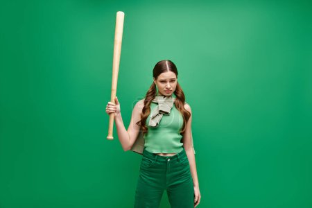 A young woman in her 20s confidently holds a baseball bat against a vibrant green background.