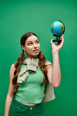 Foto de Una joven de unos 20 años sostiene un pequeño globo en su mano, contemplando la belleza y complejidad de los mundos. - Imagen libre de derechos