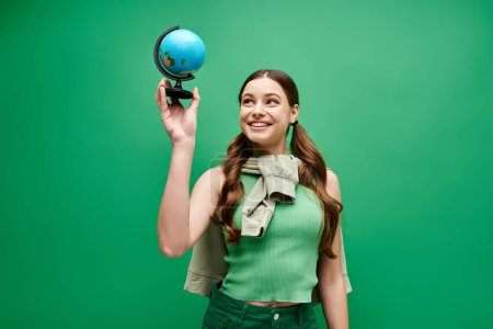 Una joven y hermosa mujer de unos 20 años está sosteniendo delicadamente un fascinante globo azul en un estudio en verde.