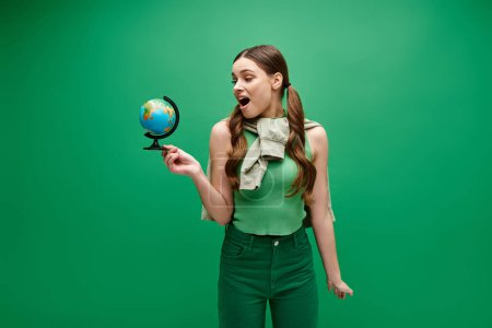 Foto de A young woman in her 20s holds a small globe in her hand, symbolizing connection and unity with the world. - Imagen libre de derechos