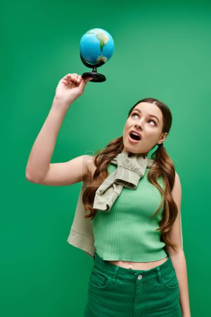 A young beautiful woman in her 20s wearing a green shirt, holding a blue globe in a studio setting.