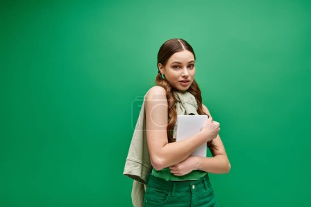 A stunning young woman in her 20s, clad in a green shirt, holds a tablet in a captivating studio setting.