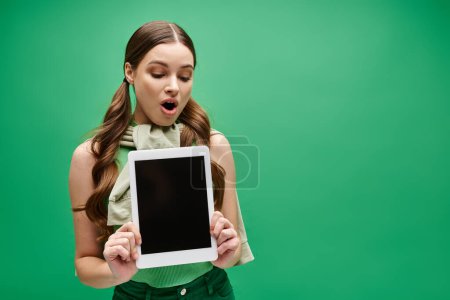 Junge Frau in ihren Zwanzigern mit einer Tablette vor dem Gesicht auf Grün