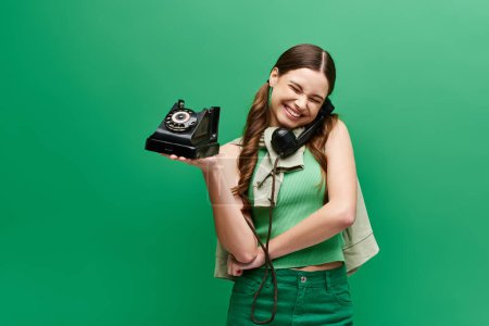 Eine junge Frau in ihren Zwanzigern hält ein Telefon in der Hand und lächelt glücklich in einem Studio mit grünem Hintergrund..