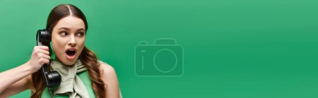 Photo for A young woman in her 20s holds a phone to her face, lost in conversation or contemplation in a studio with a green background. - Royalty Free Image