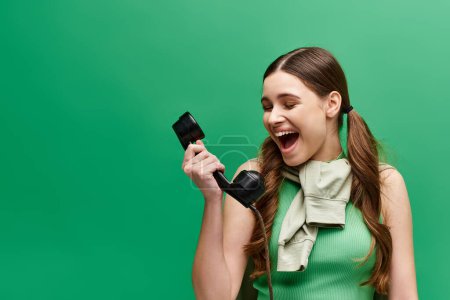 Une jeune femme dans la vingtaine tient un téléphone à l'ancienne sur son visage dans un cadre de studio, l'air nostalgique.