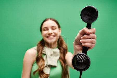 Téléchargez les photos : A young beautiful woman in her 20s holding a vintage telephone on a vivid green background. - en image libre de droit