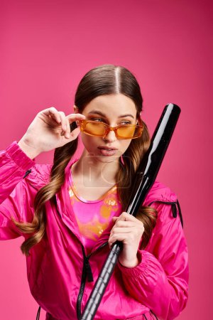 Foto de Una joven y hermosa mujer de unos 20 años posa en un estudio con una chaqueta rosa mientras sostiene un par de gafas de sol.. - Imagen libre de derechos
