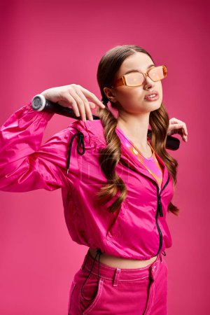 Téléchargez les photos : Young beautiful woman in her 20s wearing a pink jacket and pink pants, striking a pose in a studio setting with a pink background. - en image libre de droit