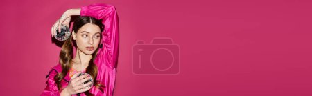 Foto de Una joven de unos 20 años, vestida con un elegante vestido rosa, se levanta con gracia sobre un vibrante fondo rosa. - Imagen libre de derechos