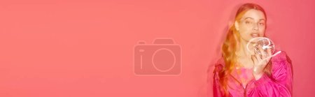 Téléchargez les photos : Une jeune femme en robe rose tient élégamment un bal disco, créant une atmosphère rêveuse et magique dans un studio avec un fond rose. - en image libre de droit