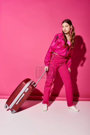 A stylish woman in her 20s holding a pink suitcase against a vibrant backdrop.