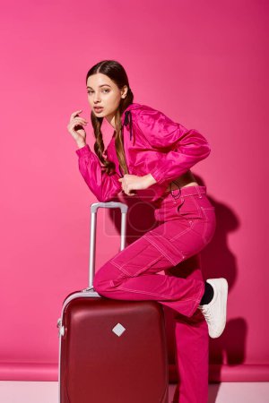 Foto de Una joven con estilo de unos 20 años posando con una maleta frente a una vibrante pared rosa. - Imagen libre de derechos