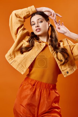 Téléchargez les photos : Jeune femme élégante dans la vingtaine posant dans un cadre de studio dynamique portant une veste jaune et un pantalon orange sur fond. - en image libre de droit
