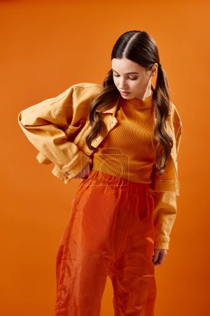 Foto de Una mujer joven y elegante de unos 20 años se levanta con gracia frente a un fondo naranja vibrante, que exuda elegancia y equilibrio.. - Imagen libre de derechos