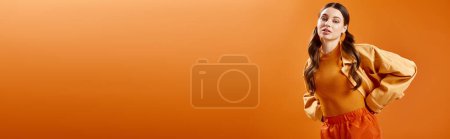 Téléchargez les photos : A young woman in her 20s wearing an orange shirt and pants against a bright orange background. - en image libre de droit