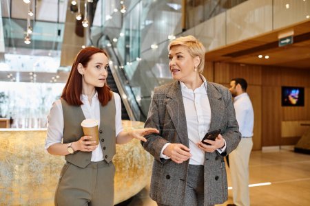 Two women engaged in conversation in a modern lobby setting.