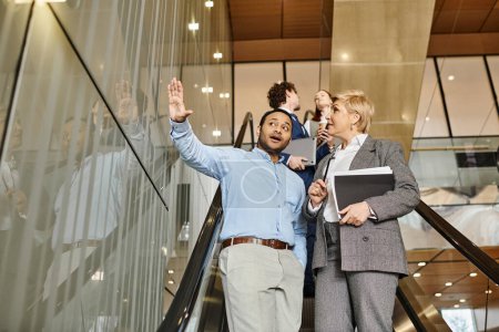 Téléchargez les photos : Un groupe diversifié de professionnels des affaires debout sur un escalier roulant dans l'unité. - en image libre de droit